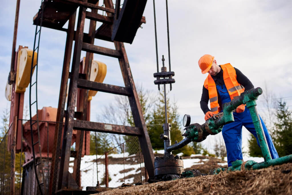 Oilfield worker in safety gear operating a pipeline valve at an oil rig site.