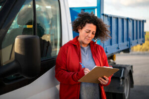 Commercial driver completing paperwork on a clipboard beside a truck.