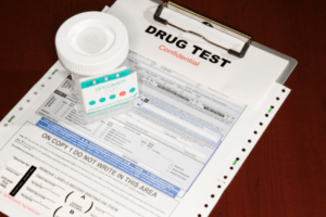 A close-up of a "Drug Test Confidential" clipboard, a federal chain of custody form, and a sealed specimen cup for a DOT-regulated urine screen.