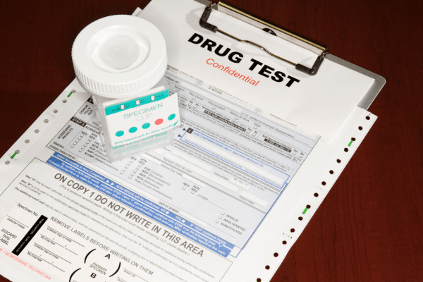 A close-up of a "Drug Test Confidential" clipboard, a federal chain of custody form, and a sealed specimen cup for a DOT-regulated urine screen.