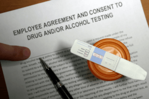 Employee agreement and consent form for drug and alcohol testing alongside a urine specimen cup and rapid test strip, representing the documentation and collection process managed through DER, TPA, and MRO coordination.
