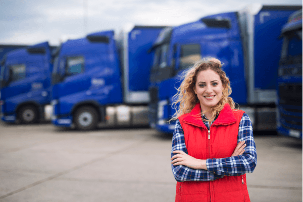 Female transportation worker standing in front of a fleet of commercial trucks with arms crossed, representing a DOT safety-sensitive employee subject to reasonable suspicion drug and alcohol testing requiremen