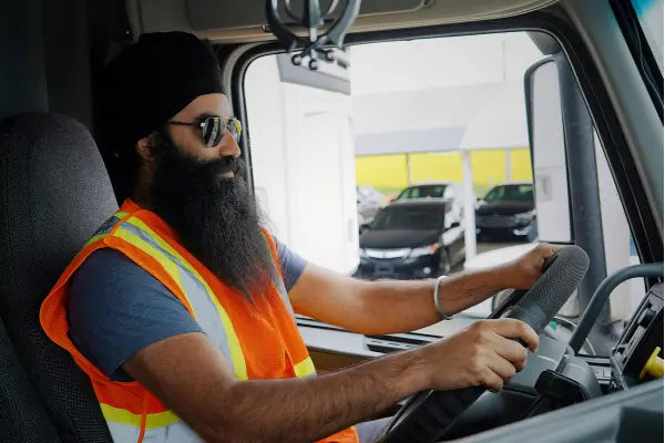 A commercial truck driver wearing a high-visibility safety vest behind the wheel of a semi-truck cab, representing the safety-sensitive roles managed by a DER.